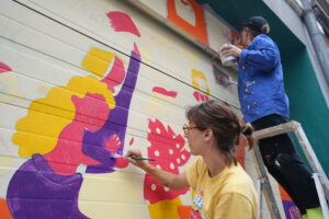 Collectif ton piquant peignant une fresque féministe sur la porte de garage d'Amazone